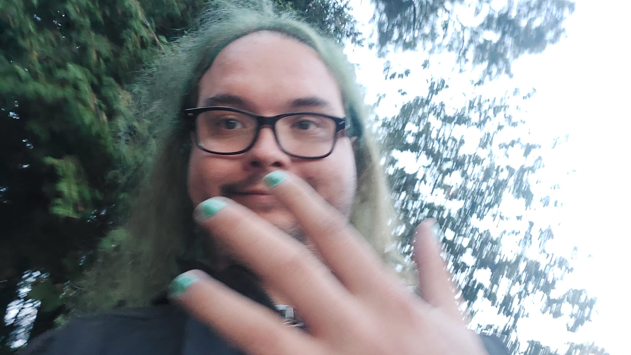 A man with long green hair and no beard shows off his green painted fingernails